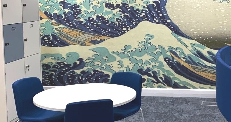 White circular table and two blue chairs in a room with a feature waves wallpaper